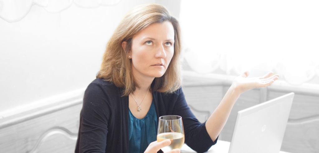 Woman with laptop looking frustrated while holding a glass of wine